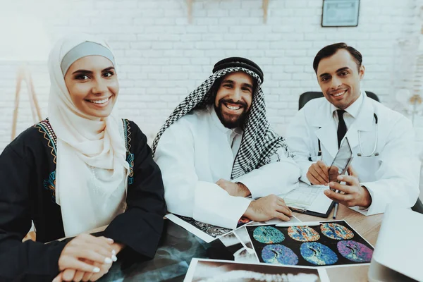 Smiling Arabic Family and Doctor Looking in Camera. Doctor Explaining Diagnosis with Tablet. Consultation at Clinic. Reception of Therapist. Discussing Diagnosis. Examination. Medical Concept.