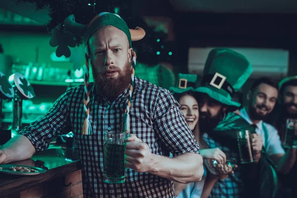 Saint Patrick\'s Day Party. Friends is Celebrating. People is Drinking a Green Beer and Eating a Nuts. Friends is a Men and Women. People in a Green Hats. Beard Man Looking into a Camera. Pub Interior.