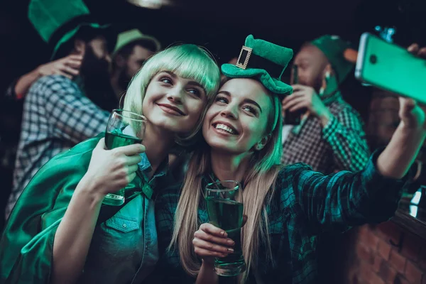 Saint Patrick\'s Day Party. Friends is Celebrating. Happy People is Drinks a Green Beer. Friends is Young Men and Women. Girls is Doing a Selfie on Cellphone. People Wearing a Green Hats. Pub Interior.