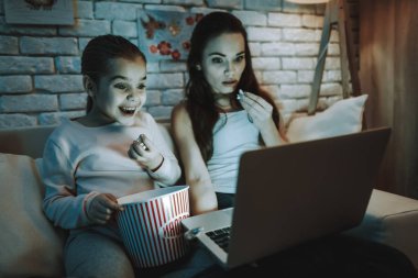 Anne ile kızı koltukta oturuyor. İnsanları dizüstü bilgisayar ile ilgili bir Video izlemek. Patlamış mısır yemek kişi. Anne şaşırır. Gülen bir kızdır. Duvar resimleri ile. Akşam saat. Ev iç.