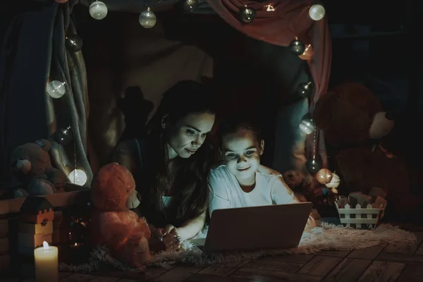 母女躺在地毯上 躺在假帐篷下的人 母亲和女儿正在使用笔记本电脑 人是快乐和微笑的 晚上的时间 家庭内部的人 — 图库照片