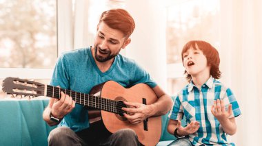 Genç oğlu ile gitar çalmaya baba sakallı. Mutlu aile kavramı. Müzisyen evde. Genç çocuk gömlek. Modern hobi kavramı. Müzik ve şarkı kavramları. Gülümseyen adam.
