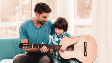 Genç oğlu ile gitar çalmaya baba sakallı. Mutlu aile kavramı. Müzisyen evde. Genç çocuk gömlek. Modern hobi kavramı. Müzik ve şarkı kavramları. Gülümseyen adam.