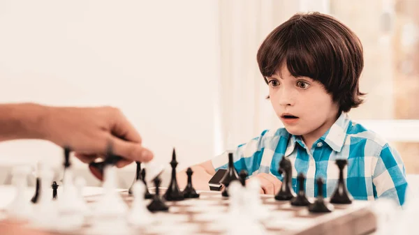 Bearded Father and Son Playing Chess on Table. Happy Family Concept. Board on Table. Young Boy in Shirt. Indoor Joy. Board Games Concept. Modern Hobby Concept. Black and White Figures.