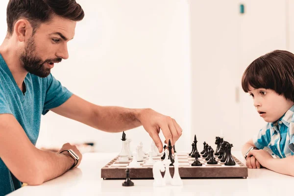 Bearded Father and Son Playing Chess on Table. Happy Family Concept. Board on Table. Young Boy in Shirt. Indoor Joy. Board Games Concept. Modern Hobby Concept. Black and White Figures.