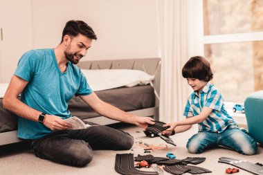 Baba ve oğul oyuncak yarış yol ile oynarken sakallı. Katta oturan adam. Beyaz halı odasında. Oyuncak arabalar. Çıktıktan çocuk. Mutlu aile kavramı. Beyaz halı. Yerde yatıyor. Kapalı eğlenceli.