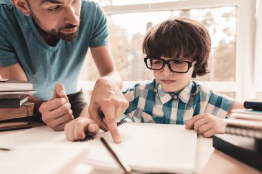 Küçük çocuk babası ile ödev gözlük. Evde eğitim. Oda beyaz tablosunda. Oturan çocuk. Genç baba. Evde ders. Eğitim kavramı. Not defterinde yazılı. Çocuk gömlek.