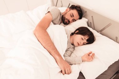 Yatakta yorgun uyuyan babası ile küçük oğlu.
