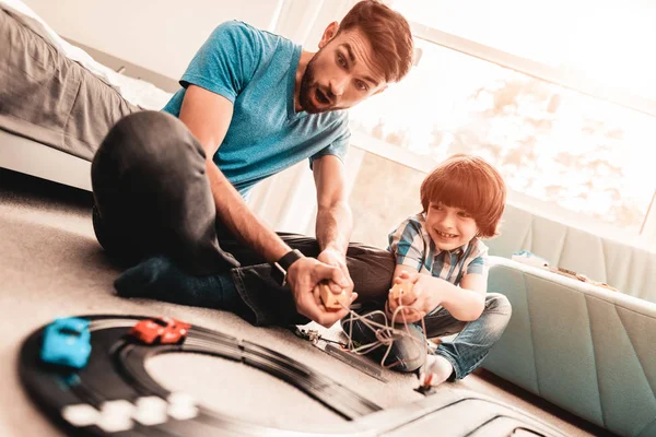 Bearded Father and Son Playing with Toy Race Road. Man Sitting on Floor. White Carpet in Room. Toy Cars. Exited Boy. Happy Family Concept. White Carpet. Lying on Floor. Indoor Fun.