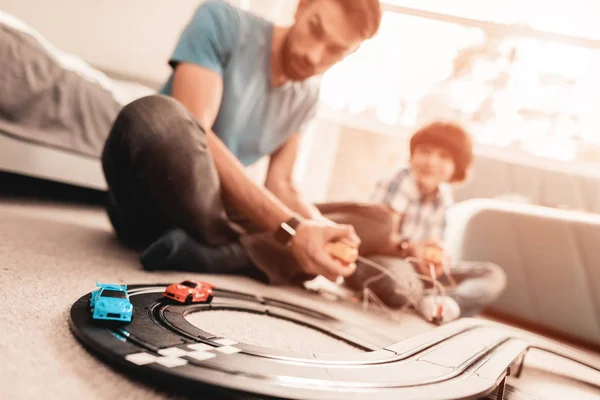 Bearded Father and Son Playing with Toy Race Road. Man Sitting on Floor. White Carpet in Room. Toy Cars. Exited Boy. Happy Family Concept. White Carpet. Lying on Floor. Indoor Fun.