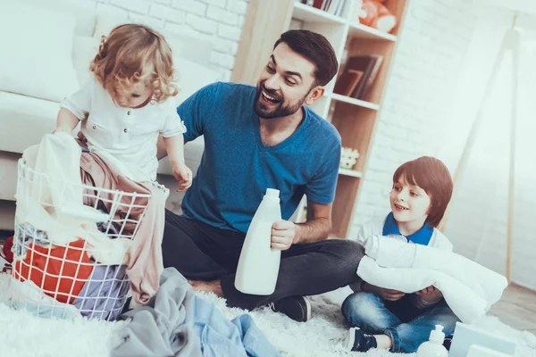 Man Spends Time with His Sons. Father is Engaged in Raising Children. Father is Teaching a Sons a Cleaning. People Want to Wash a Dirty Clothes. People is Located in Bedroom on Carpet.