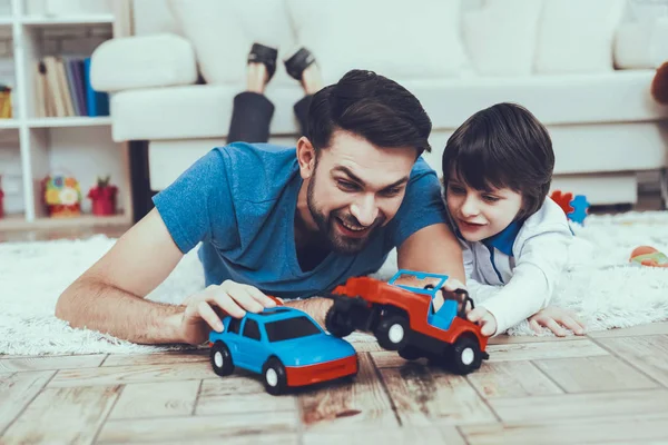 Man Spends Time with His Son. Father of Boy is Engaged in Raising Child. Father and Son is Playing with Toy Cars. Persons is Lying on Carpet and Smiling. People is Located in Bedroom.