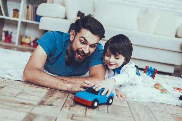 彼の息子との時間を費やしています 少年の父を上げる子で行っています 父と息子は おもちゃの車で遊んでいます 人はカーペットに横たわると笑顔です 寝室にあります — ストック写真