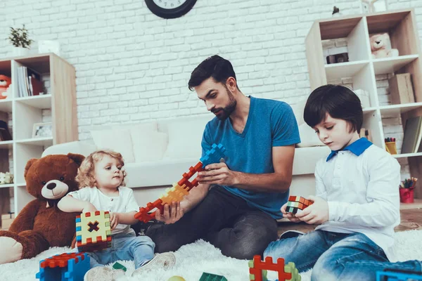 彼の息子との時間を費やしています 父親は子育てに取り組んでいます 父と息子は おもちゃで遊んでいます 長男は ルービック キューブを保持しています 寝室のカーペットに座っています — ストック写真