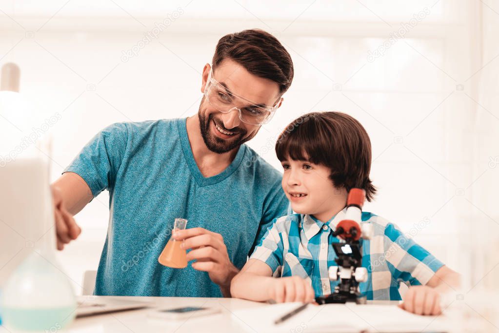 Youn Bearded Father Teaching Son in Shirt at Home. Education at Home. Using Microscope. Studding Chemistry. White Table in Room. Sitting Boy. Young Father. Lesson at Home. Education Concept.