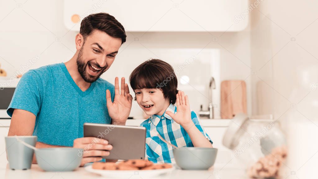 Happy Young Father and Son Using Tablet at Home. Smiling Boy. Modern Kitchen. Sitting Boy. Boy in Shirt. Breakfast in Morning. White Table in Kitchen. Using Digital Device. Happy Family.