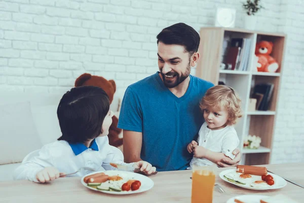 彼の息子との時間を費やしています 男の子のお父さんは 子育てに取り組んでいます 息子に朝食を給餌します テーブルで椅子に座っています キッチンにある人々 — ストック写真