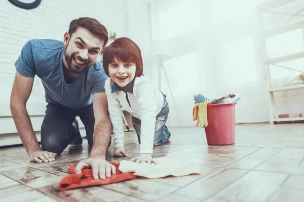 Man Spends Time with His Son. Father is Engaged in Raising Child. Father is Teaching a Son a Cleaning. Father and Son Washing the Floor with Rags. Persons is Smiling. People is Located in Bedroom.