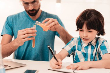 Youn evde baba öğretim oğul gömlekli sakallı. Evde eğitim. Mikroskop kullanarak. Öğrendiğim kimya. Oda beyaz tablosunda. Oturan çocuk. Genç baba. Evde ders. Eğitim kavramı.