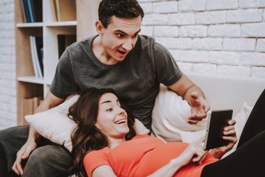 Çift Video izlerken Tablet Pc. çift üzerinde bir erkek ve hamile kadın olmasıdır. Mutlu ve Surprised kişidir. Kadın dokunmadan bir Tablet ekranıdır. İnsanlar kanepede. Evde bulunan insanlar.