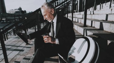 İşadamı bir Tablet Pc. işadamı kullanarak eski gülümseyen adam adam bir fincan kahve Holding. Siyah takım elbise giyen adam. İşadamı merdiven üzerinde oturuyor. Monowheel yakınındaki bir adam güneşli gündüz.