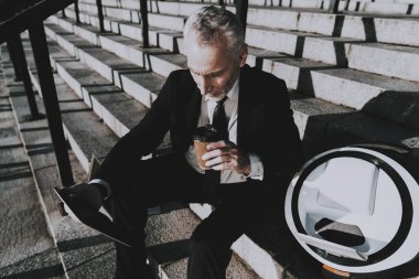 İşadamı bir Tablet Pc. işadamı kullanarak eski gülümseyen adam adam bir fincan kahve Holding. Siyah takım elbise giyen adam. İşadamı merdiven üzerinde oturuyor. Monowheel yakınındaki bir adam güneşli gündüz.