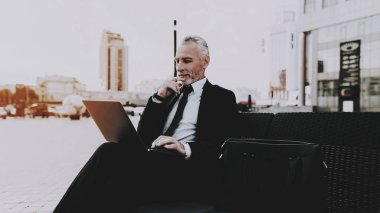 İşadamı bir dizüstü bilgisayar kullanıyor. İşadamı Laptop ekranında arıyor. Eski gülümseyen adam adam siyah elbiseli işadamıdır. Evrak Çantası'nı bir adam işadamı yakınındaki kanepede oturuyor. Gündüz.