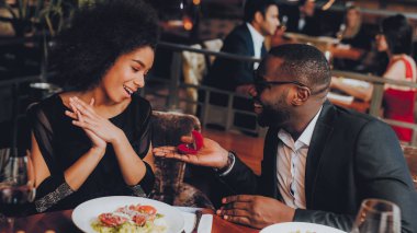 Kız arkadaşıma evlenme teklif Afrika yakışıklı adam. Aşk dating romantik çift. En adam ve kız bir restoranda. Romantik kavramı. Bir evlenme teklifi almak çekici kadın şaşırttı.