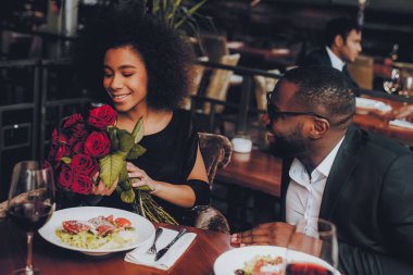 Afrika kökenli Amerikalı çift restoranda. Aşk dating romantik çift. En adam ve kız bir restoran yapma sırayla. Romantik kavramı. Adam buket çiçek vererek. Kırmızı gül.