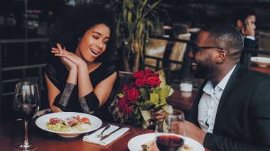 Afrika kökenli Amerikalı çift restoranda. Aşk dating romantik çift. En adam ve kız bir restoran yapma sırayla. Romantik kavramı. Adam buket çiçek vererek. Kırmızı gül.