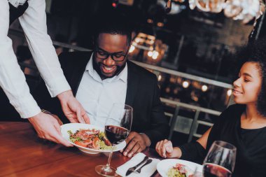Salata Afrikalı çift lokantaya hizmet garson. Aşk dating romantik çift Afro-Amerikan. Neşeli erkek ve kadın kırmızı şarap içme. Romantik kavramı. Yıldönümü. Bardak kırmızı şarap.