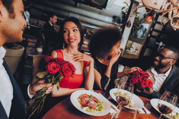 Friends in a Restaurant Enjoying Romantic Evening. Group Happy Friends Enjoying Dating in Restaurant. Double Couple Dating in Restaurant. Romantic Concept. Bouquet Red Roses. Love Concept.