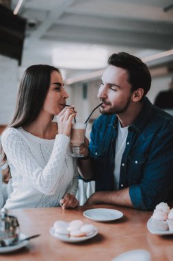 Cafe dinlenme çift. İki güzel genç erkek ve kadın var. Çift bir Latte üzerinden bir Kupası birlikte içiyor. Kişi masada oturuyor. Mutlu ve gülen kişidir. Güneşli gün.