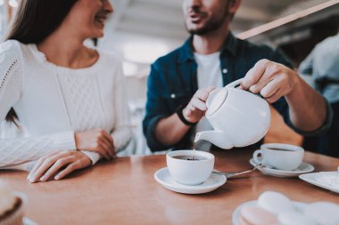 Cafe dinlenme çift. İki güzel genç erkek ve kadın var. Adam bir çay üzerinden su ısıtıcısı için kadın yağıyor. Kişi masada oturuyor. Mutlu ve gülen kişidir. Güneşli gün.