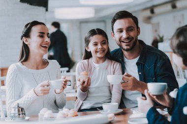 Aile Cafe dinleniyor. Anne, Baba, kızı ve oğlu ailedir. Yemek kek ve bir çay içme kişidir. Kişi masada oturuyor. Mutlu ve gülen kişidir. Güneşli gün.