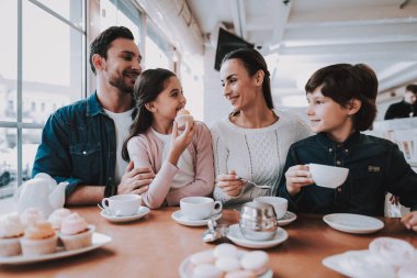 Aile Cafe dinleniyor. Anne, Baba, kızı ve oğlu ailedir. Yemek kek ve bir çay içme kişidir. Kişi masada oturuyor. Mutlu ve gülen kişidir. Güneşli gün.
