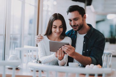 Cafe dinlenme çift. İki güzel genç erkek ve kadın var. Çift bir Tablet Pc. kullanarak kişi masada oturuyor. Mutlu ve gülen kişidir. Kek ve çay tablo. Gündüz.