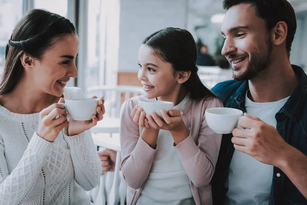Aile Cafe dinleniyor. Anne, baba ve kızı ailedir. İnsanlar bir bardak tutan ve bir çay içme. Kişi masada oturuyor. Mutlu ve gülen kişidir. Güneşli gün.