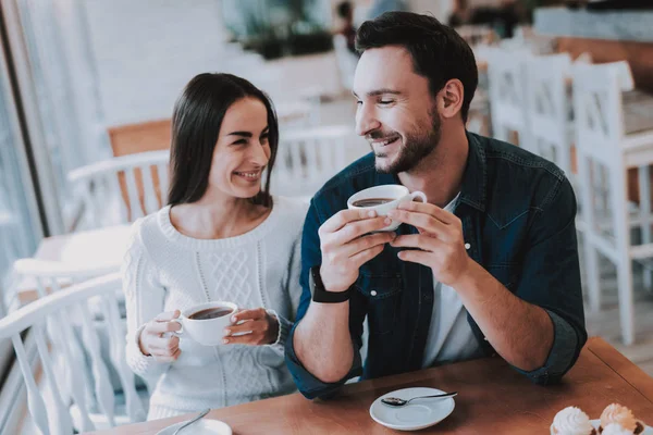 Couple Resting in Cafe. Couple is Beautiful Young Man and Woman. Couple is Drinking Tea. People is Looking on Each Other. Persons is Sitting at Table. People is Happy and Smiling. Daytime.