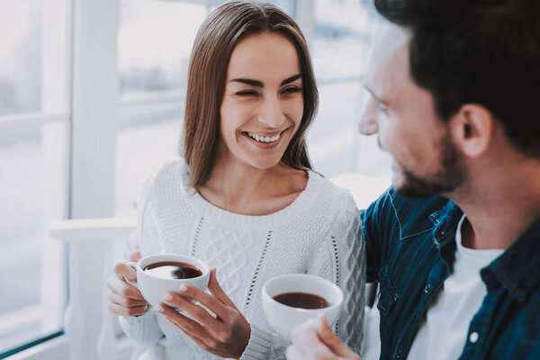 Happy Couple Resting in Cafe. Couple is Beautiful Young Man and Woman. Persons is Sitting at Table. People is Smiling to Each Other. People is Drinking a Tea From Cups. Sunny Daytime.