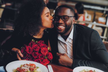 Afrika kökenli Amerikalı çift restoranda. Aşk dating romantik çift. En adam ve kız bir restoran yapma sırayla. Romantik kavramı. Adam buket çiçek öpüşme kız. Kırmızı gül.