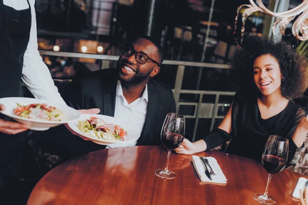 Salata Afrikalı çift lokantaya hizmet garson. Aşk dating romantik çift Afro-Amerikan. Neşeli erkek ve kadın kırmızı şarap içme. Romantik kavramı. Yıldönümü. Bardak kırmızı şarap.