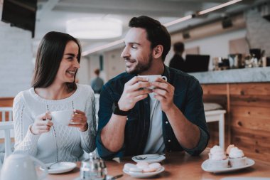Couple Resting in Cafe. Couple is Beautiful Young Man and Woman. Couple is Drinking Tea. People is Looking on Each Other. Persons is Sitting at Table. People is Happy and Smiling. Daytime.