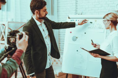 Blogcular bir Video yapar. Blogcular iş adamı ve iş kadını var. Video ile ilgili bir iş. Operatör bir Video kameraya ateş eder. Adam iş grafikte gösterilen. Bir defter tutan kadın. Studio iç.