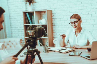 Blogger bir Video yapar. Blogger işkadını olduğunu. Video ile ilgili bir iş. Adam işleç bir Video kameraya ateş eder. Dizüstü bilgisayar ve malzemeleri masada. Bir kameraya gösteren kadın. Studio iç insanlarda.