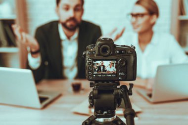 Blogcular bir Video yapar. Blogcular genç gülümseyen erkek ve kadın var. Video ile ilgili bir iş. Kamera bir Video vuruyor. Dizüstü bilgisayarlar ve malzeme masada. Studio iç insanlar. İnsanlar görüntü bulanıklığı.