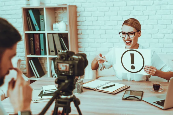 Blogger Makes a Video. Blogger is Smiling Businesswoman. Video About a Business. Man Operator Shoots a Video on Camera. Laptop and Supplies on Table. Woman Holding a Exclamation Mark. Studio Interior.