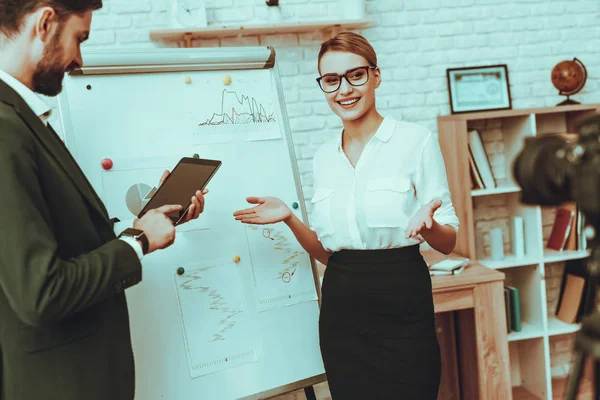 Bloggers Makes a Video. Bloggers is Businessman and Businesswoman. Video About a Business. Camera Shoots a Video. Man Showing a Tablet. Business Graph. People in Studio Interior.