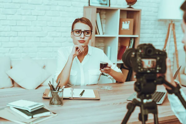 Blogger Makes a Video. Blogger is Upset Businesswoman. Video About a Business. Man Operator Shoots a Video on Camera. Laptop and Supplies on Table. Woman Drinking a Tea. People in Studio Interior.