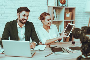 Blogcular bir Video yapar. Blogcular gülümseyen genç erkek ve kadın var. Video ile ilgili bir iş. Kamera bir Video vuruyor. Becerikli alet ve malzemeleri masada. Kadın bir Tablet kullanıyor. Studio iç insanlarda.